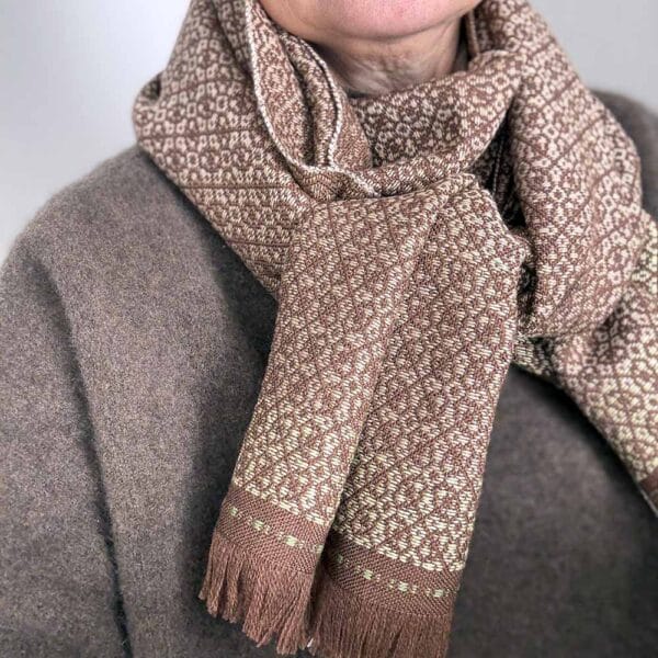 Ekslusivt håndvævet brunt tørklæde i merinould og med feminint daldrejl-mønster i beige nuancer, og lys gule og grønne detaljer i afslutningen af tørklædet.