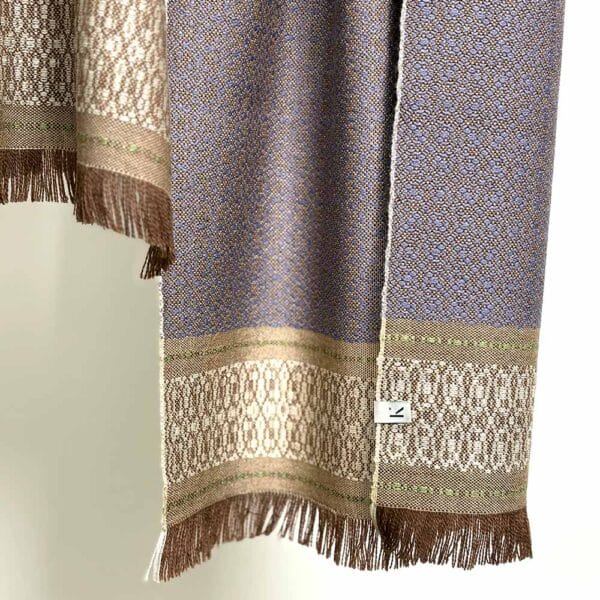 Ekslusivt håndvævet brunt tørklæde i merinould og med feminint daldrejl-mønster i blålige nuancer, og lyse detaljer i afslutningen af tørklædet.