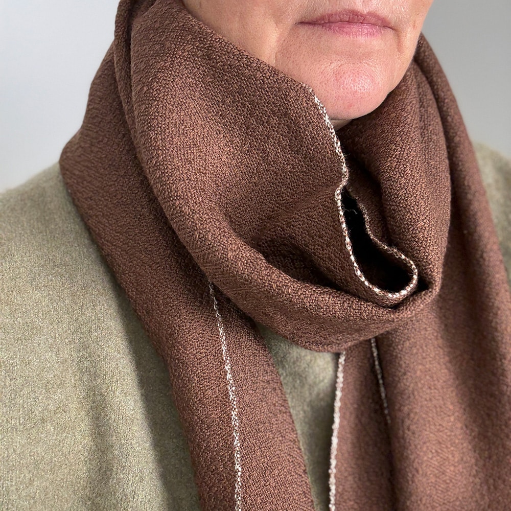 Ekslusivt håndvævet brunt tørklæde i merinould. Det er vævet brunt i brun ti et smukt mønster med lyse kanter der giver tørklædet karakter.