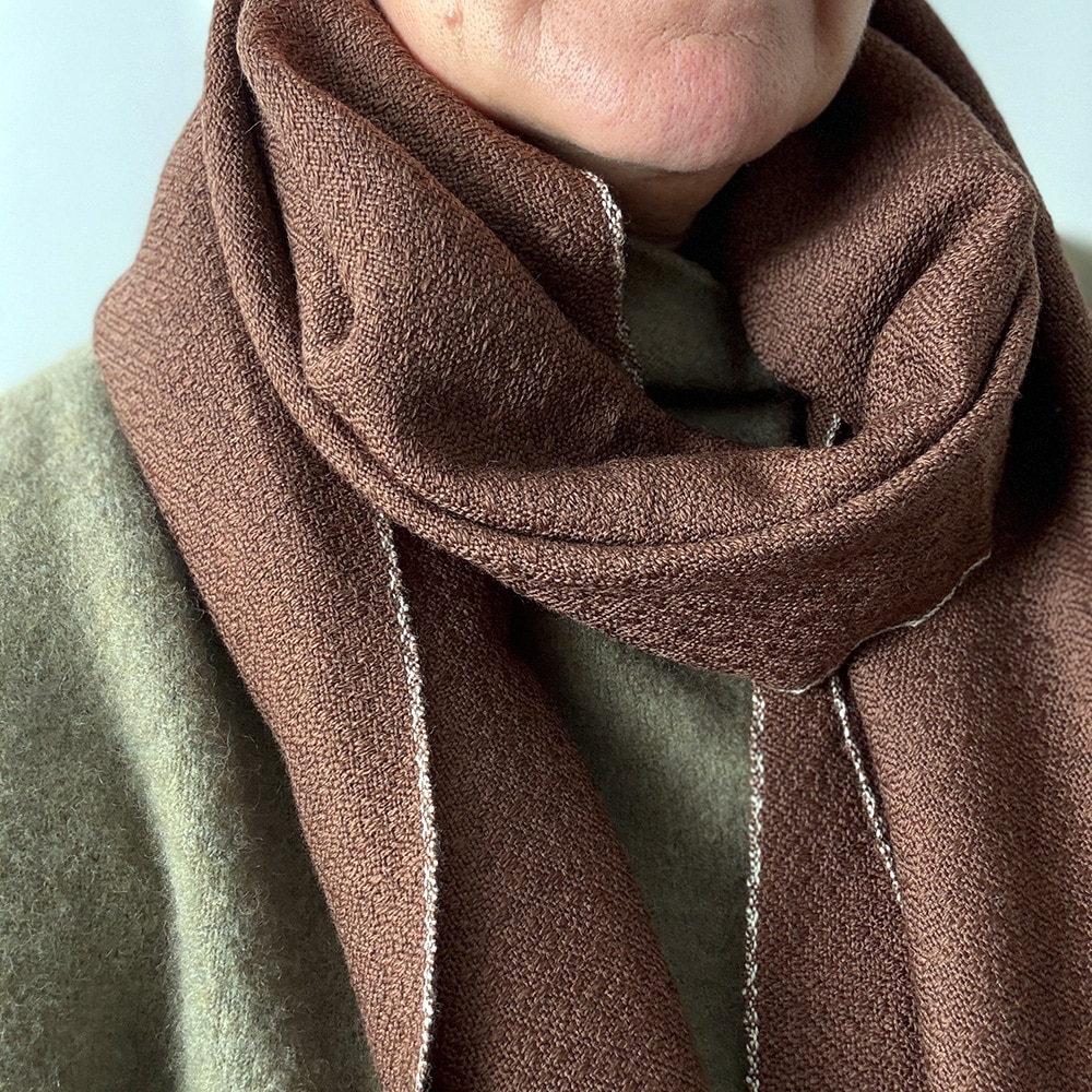 Ekslusivt håndvævet brunt tørklæde i merinould. Det er vævet brunt i brun ti et smukt mønster med lyse kanter der giver tørklædet karakter.