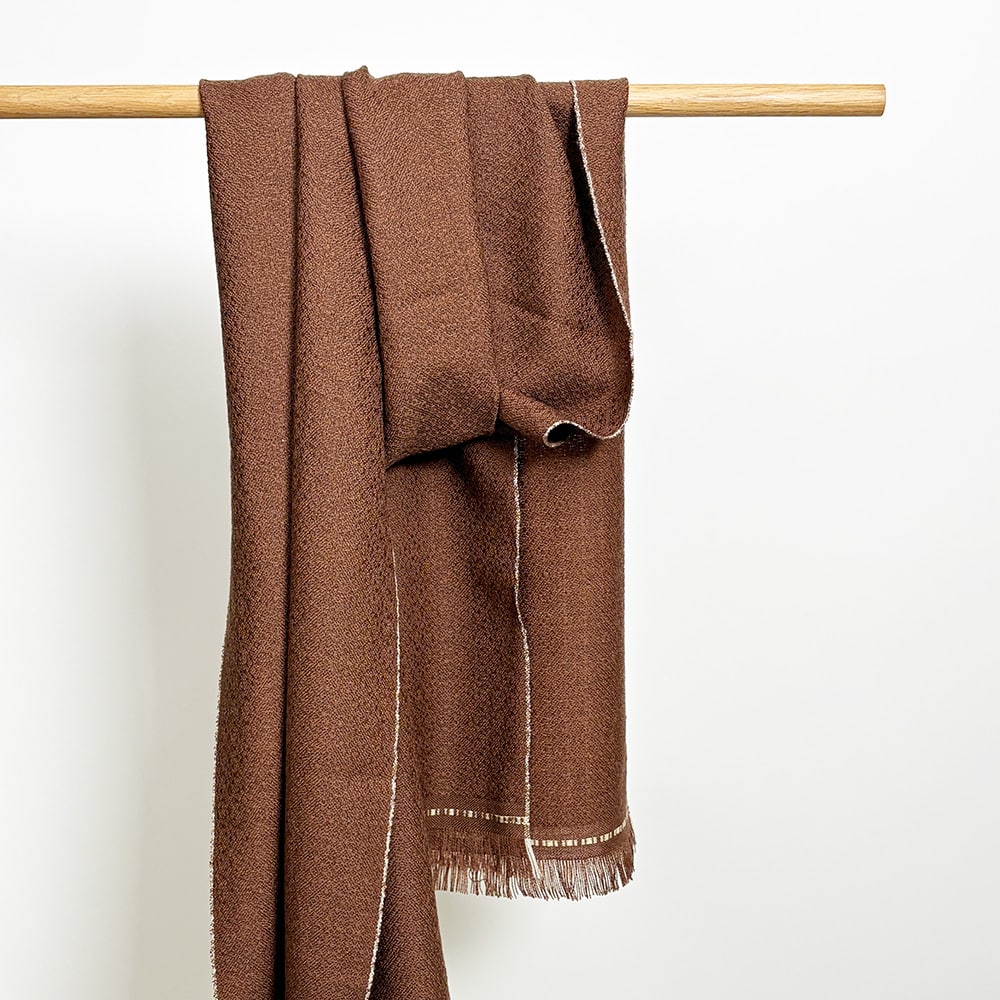 Ekslusivt håndvævet brunt tørklæde i merinould. Det er vævet brunt i brun ti et smukt mønster med lyse kanter der giver tørklædet karakter.